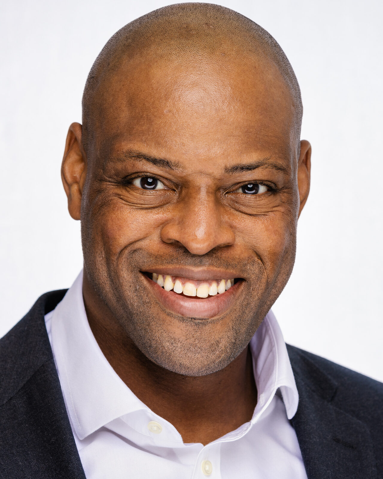 Actor headshot of Johann in a dark suit, wide smile