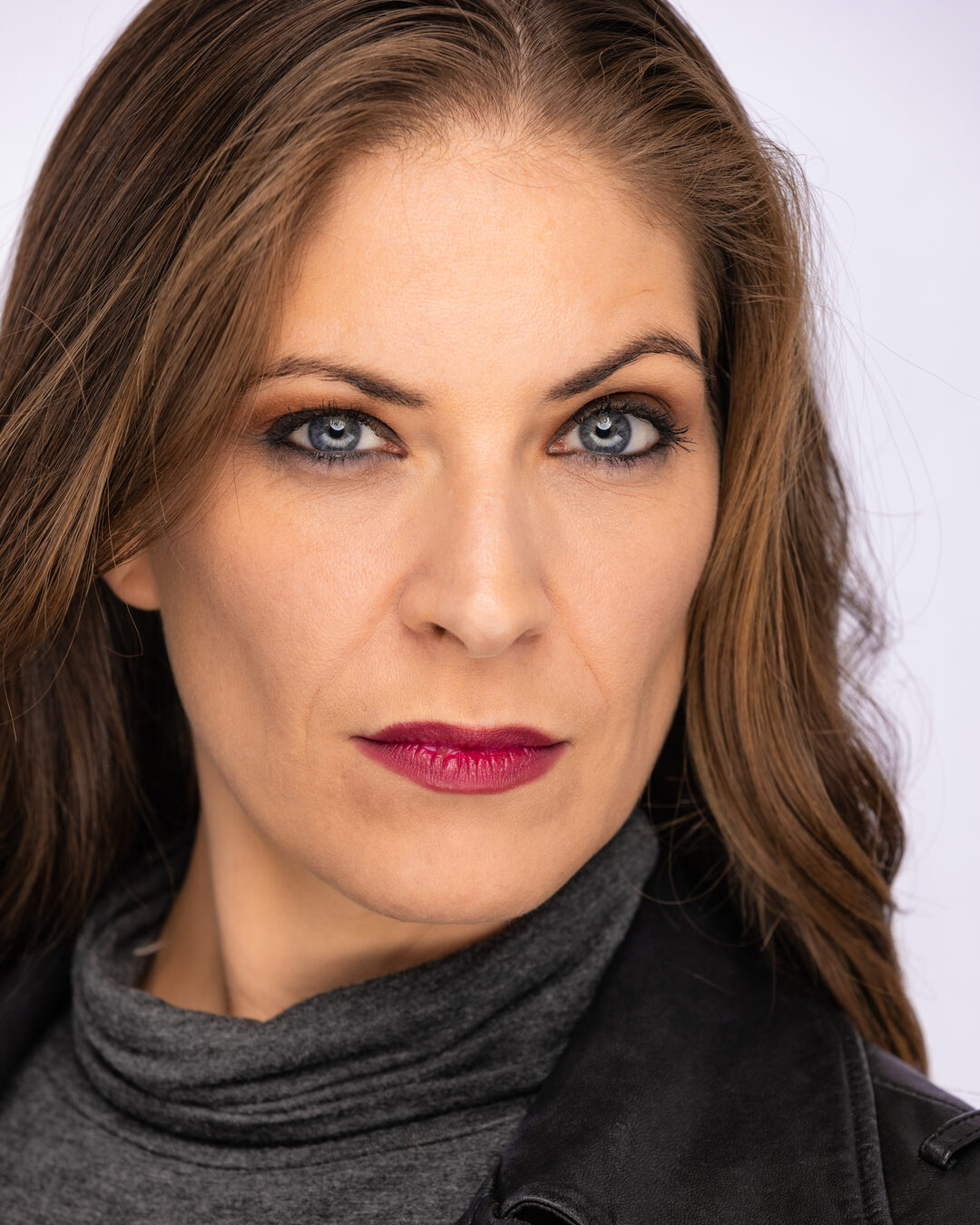 Cat in a black leather jacket over a gray turtleneck, tight crop, hard direct stare