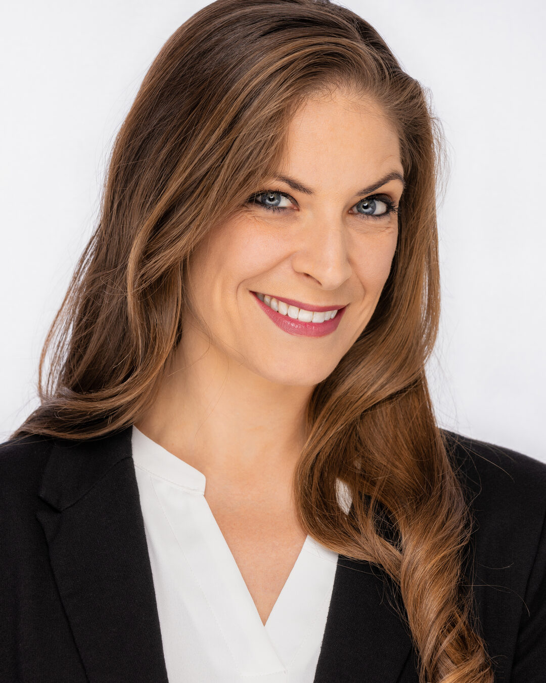 Cat with a warm three-quarter smile, hair over one shoulder, black blazer and white blouse